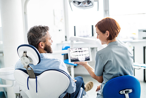 The image shows a dental office setting where a dentist is seated in a chair with a patient, both facing each other.