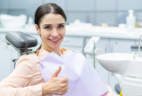 A woman in a dental office, smiling and giving a thumbs-up sign.