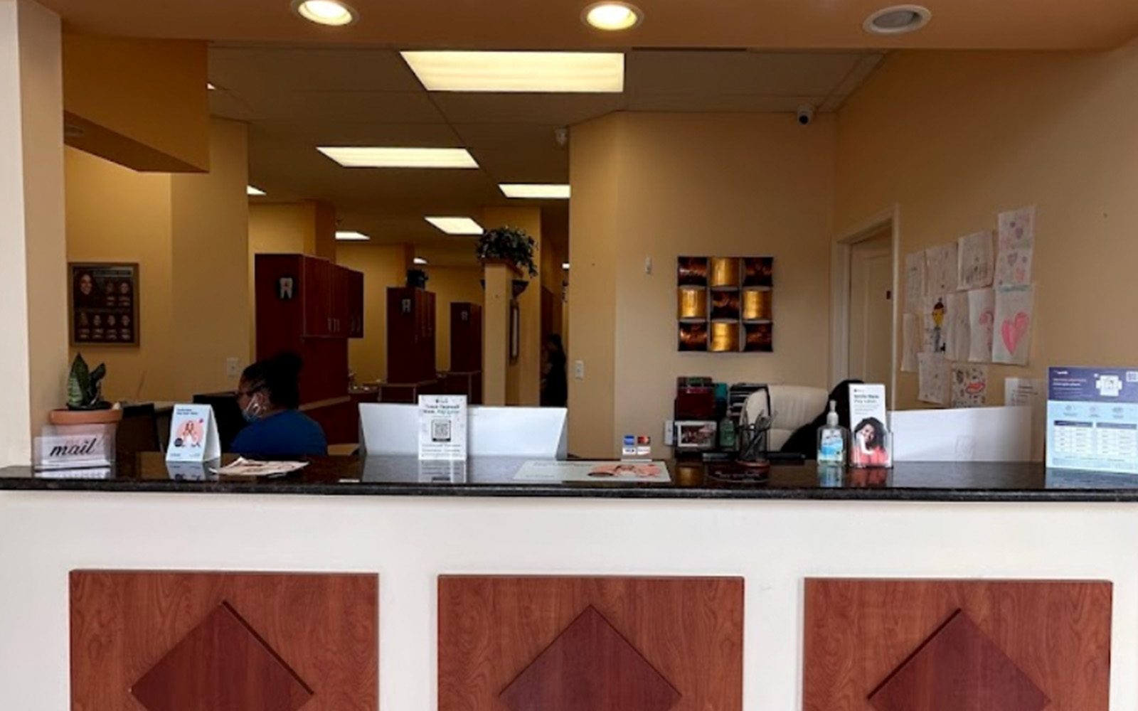 The image shows an interior view of a well-lit lobby with a reception desk, featuring three monitors and a sign.